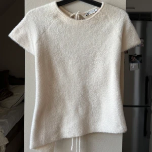 Vit topp med fuskpäls och knytning i ryggen - Supermjuk vit topp med korta ärmar i fuskpälsmaterial. Snygg detalj med knytning i ryggen som ger en unik look. Perfekt för dig som vill ha något annorlunda och trendigt. 💕 Vanligtvis en S/M men pga knytningarna i ryggen kan man justera storleken 
