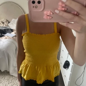 Gul smockad linnetopp med volang - Säljer en söt gul linnetopp med smockad överdel och volang nertill. Knappt använd!