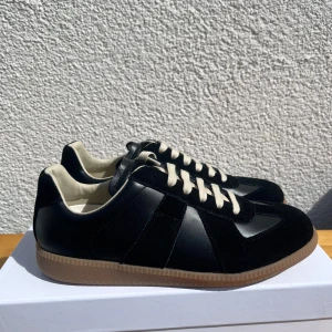 Maison Margiela - Snygga svarta sneakers med både mocka och skinnpaneler, beige snörning och bruna yttersulor. Perfekta till sommaren