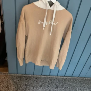 Beige hoodie med vit huva och text - Säljer en beige hoodie med vit huva och dragsko. På bröstet står det 'Ready? Ready!' i vit text. Perfekt för en avslappnad stil och superbekväm att ha på sig.