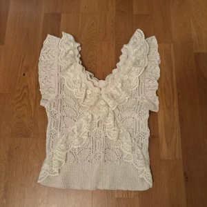 Zara volangtopp - Säljes då den ej riktigt är min stil 🤗Supersöt vit stickad topp med korta ärmar och dekorativa spetsvolanger framtill. Toppen har ett vackert mönster och djup v-ringning. Perfekt för dig som gillar romantisk stil och fina detaljer.