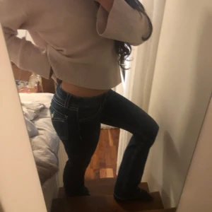Mörkblå lågmidjade bootcut jeans med vita sömmar - Säljer ett par mörkblå jeans med bootcut passform och tydliga vita sömmar. Byxorna har låg midja och klassiska fickor både fram och bak, med dekorativ knapp på bakfickan. Perfekta för dig som gillar en 2000s jeansstil.💗