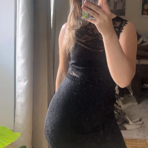 Svart spetsklänning med blommönster - Säljer en svart klänning med vacker spets och blommigt mönster. Klänningen har hög halsringning och är ärmlös, med genombrutna detaljer upptill. Perfekt för dig som gillar en elegant och feminin stil.