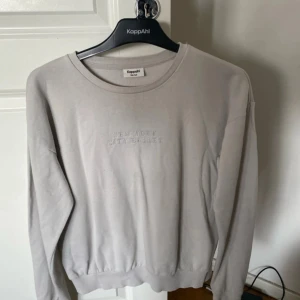 Beige sweatshirt från KappAhl med text - Säljer en beige sweatshirt från KappAhl med broderad text 'New York City Ballet' framtill. Tröjan har rund halsringning och långa ärmar, perfekt för en avslappnad stil.