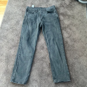 Grå Levis 541 - Säljer ett par klassiska grå jeansbyxor från Levi's med rak passform. Byxorna har fem fickor, bälteshällor och knappgylf. Perfekta för dig som gillar en tidlös och enkel stil. Storlek 34/32