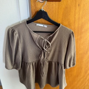 Beige blus med knytning - Säljer en beige blus med puffärmar och knytning framtill. Blusen har en lös passform och är tillverkad i ett mjukt, strukturerat material. Perfekt för dig som gillar en avslappnad men ändå söt stil.