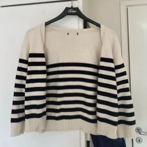 Randig kofta i stickat material - Säljer en krämvit och svart randig kofta i stickat material. Koftan har trendiga terkvartds ärmar med knappar framtill. Perfekt att slänga över ett linne eller t-shirt för en chill look.