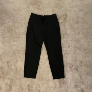 Svarta kostymbyxor från H&M Regular Fit - Säljer ett par svarta kostymbyxor från H&M i modellen Regular Fit. Byxorna har klassisk passform med hällor för bälte och stängs med dragkedja och knapp. Perfekta för en stilren look.