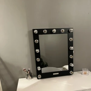 Svart sminkspegel med LED-lampor - En rektangulär sminkspegel med svart ram och tolv stora LED-lampor runt. Spegeln är ifrån bridge mode och ny pris 2200kr. Spegeln har inga effekter eller hål eller märken. För mer frågor eller bilder kom privat. Spegeln är 50x60 den är dimm bar