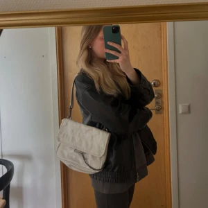 Vit axelväska med kedjedetalj - Säljer en stilren vit axelväska med silverfärgad kedja och lock. Väskan har en klassisk rektangulär form och är perfekt för att bära det viktigaste. Enkel och snygg design som passar till många outfits. Från zara och är rejäl i materialet.