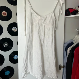 Klänning med knytaxelband - Säljer en söt vit kortklänning med tunna knytaxelband. Klänningen har en luftig och avslappnad passform, perfekt för varma dagar. Materialet känns mjukt och somrigt. Storlek M men är för liten för mig så skulle säga S.