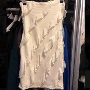 Vit volangklänning från Oh Polly - Supersnygg vit klänning från Oh Polly med volangdetaljer som går diagonalt över hela klänningen. Axelbandslös modell med figurnära passform och kort längd. Silikonkant som gör att klänningen inte åker ner. Aldrig använd, endast testas.