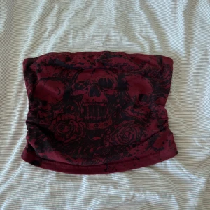 Vinröd tubhalsduk med dödskallemönster - Cool vinröd tubhalsduk med svart dödskalle- och rosmönster. Perfekt accessoar för dig som vill sticka ut och addera lite edge till din stil. Mjuk och skön att bära under kyliga dagar.