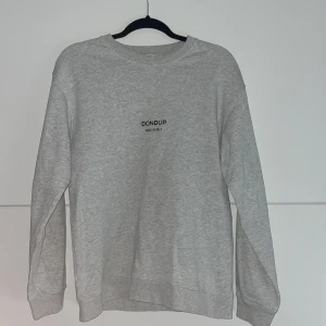 Grå sweatshirt från Dondup - Säljer en stilren grå sweatshirt från Dondup med diskret logga på bröstet. Tröjan har rund halsringning och långa ärmar. Perfekt för en avslappnad och trendig look.
