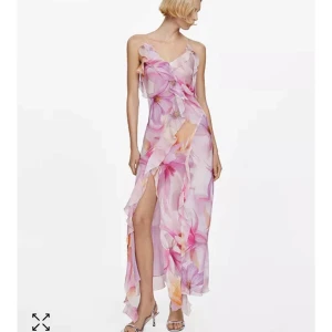 Lång blommig klänning från Mango - Kanske din balklänning? Helt slutsåld Superfin långklänning från Mango i ett tunt, flowy material med stora blommor i rosa, lila och orange toner. Klänningen har volangdetaljer, slits framtill, smala axelband och öppen rygg med knyt. Perfekt för sommarens alla tillfällen!
