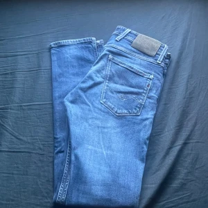 Replay Anbass W32/L32 - Säljer ett par klassiska blå jeans från Replay med fem fickor och normal passform. Jeansen har snygga slitningar och detaljer vid fickorna. Perfekta till vardags och passar till det mesta. Stängs med dragkedja och knapp. Skicket är 10/10, storlek W32 L32 slim fit 