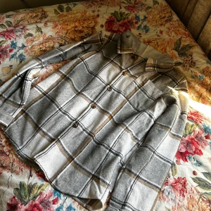 Grå och beige rutig skjorta - Säljer en snygg rutig skjorta i grått och beige med svarta linjer. Skjortan har klassisk krage, långa ärmar och knäppning framtill. Perfekt för dig som gillar en avslappnad men ändå stilren look.