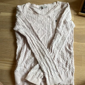 Ljusrosa kabelstickad tröja från Flash Woman - Säljer en ljusrosa kabelstickad tröja från Flash Woman i storlek M. Tröjan har v-ringning, långa ärmar och ett diskret broderat märke på bröstet. Perfekt för lager-på-lager och passar till många olika stilar.