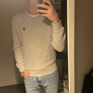 Ljusgrå sweatshirt från Lyle & Scott - Säljer en stilren ljusgrå sweatshirt från Lyle & Scott med deras klassiska gula logga på bröstet. Tröjan har rund halsringning och långa ärmar. Perfekt för en avslappnad och snygg look.