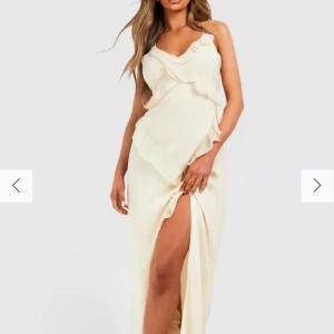 Långklänning med volang och slits - Säljer en elegant klänning med volangdetaljer och slits framtill. Klänningen har smala axelband, öppen rygg med knytning och dragkedja vid sidan. Perfekt för bal, examen, festliga tillfällen eller helt enkelt sommaren. Den är NY, ENDAST TESTAD (beställde två storlekar från Boohoo). Storlek M-L (42) för mig som har 40 i storlek passade denna bra.