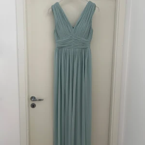 Ljusgrön långklänning med v-ringning - Elegant ljusgrön långklänning med djup v-ringning och veckade detaljer både fram och bak. Klänningen har breda axelband och ett fint fall i kjolen, perfekt för speciella tillfällen. Är 174 och ändå ner till marken på mig 