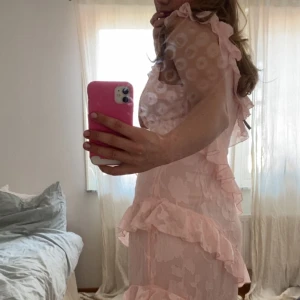 Ljusrosa långklänning med volanger från Boohoo - Supersöt ljusrosa långklänning från Boohoo med volangdetaljer och blommigt mönster. Aldrig använd, köpte förra året. Passar mig som har storlek 38. 