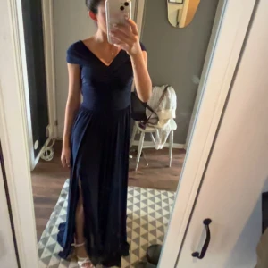 Mörkblå långklänning med slits - Elegant mörkblå långklänning med v-ringad omlott-topp och korta ärmar. Klänningen har en hög slits framtill och draperad midja som ger en smickrande siluett. Perfekt för speciella tillfällen. Bara använd en gång. Skriv för flera bilder eller frågor! 🤗