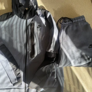 Grå blå mjukisbyxor från Nike - Snygga grå mjukisbyxor från Nike med svart logga på vänster ben. Byxorna har dragsko i midjan och är perfekta för en avslappnad stil eller träning. Matchar med hoodie i samma färg. I väldigt bra sick 