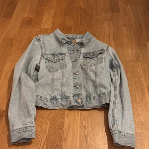 Ljusblå croppad jeansjacka från 157 - Säljer en ljusblå croppad jeansjacka från 157 med klassisk krage och knäppning framtill. Jackan har två bröstfickor med lock och knappar samt långa ärmar. Perfekt för vår och sommar!