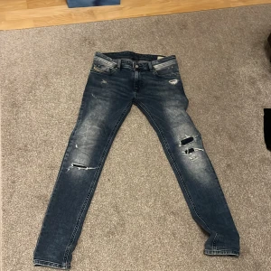 Blå slitna jeans från Diesel - Säljer ett par blå jeans från Diesel med slitna detaljer och hål på benen. Jeansen har klassisk femficksdesign och raka ben. Perfekta för en avslappnad och trendig look. Nypris: 1500 Mitt pris: 700