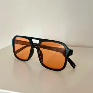 Svarta solglasögon med orange glas - Snygga solglasögon med svart, kantig båge och stora fyrkantiga orangefärgade glas. Perfekt accessoar för att sticka ut och ge en cool retrovibe till din stil🤵🏼