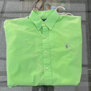 Ralph Lauren skjorta – ljusgrön, slim fit, stl L - Superfin Ralph Lauren herrskjorta i ljusgrönt – en klassisk färg som funkar året runt. Modellen är slim fit och sitter snyggt utan att bli för tajt. Perfekt både till vardags, jobb eller mer uppklätt! Skjortan har den ikoniska broderade Polo-loggan på bröstet och är tillverkad i 100 % bomull för en skön och luftig känsla. 	•	Storlek: L 	•	Passform: Slim fit 	•	Färg: Ljusgrön 	•	Material: 100 % bomull 	•	Skick: Bra – sparsamt använd, inga defekter  Passar perfekt för dig som gillar märkeskläder, 