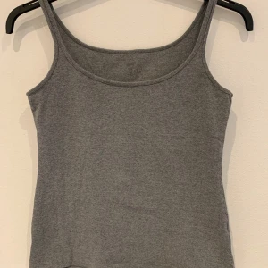 Grå ribbad linnetopp från H&M - En enkel och stilren grå ribbad linnetopp från H&M. Toppen har smala axelband och rundad halsringning, perfekt för varma dagar eller som lager under andra plagg.