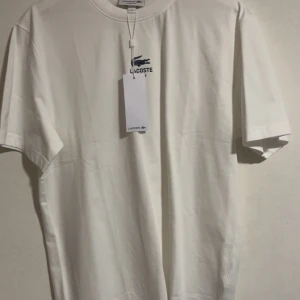 Vit t-shirt från Lacoste - Super snygg Lacoste t-shirt i top skick. Sällsynta och går inte länge att få tag på. Skick : helt ny aldrig använd. Tag sitter frf kvar. Strl M men passar S. Köpt i paris för 750 kr. Mitt pris 499. 