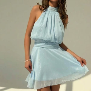 Ljusblå halterneck klänning - Säljer en ljusblå kortklänning med halterneck och lätt glittrigt tyg. Den är helt oanvänd därför den passar inte mig.