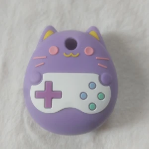 Lila katt tamagotchiskal med spelmotiv - Supergullig liten tamagotchi i lila silikon formad som en katt med spelkontroll på magen. Har söta detaljer som öron, morrhår och små färgade knappar. Vet inte vilken den passar till...