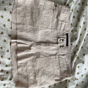Beige miniskirt med broderi från Marc Lauge Italy - Snygg beige kortkjol från Marc Lauge Italy med dekorativa broderier på fram- och bakfickor. Silvriga knappar framtill och ficklock bak. Midjan är insydd så skriv till mig om du undrar över mått❤️