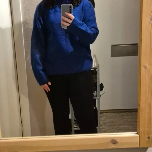 Blå stickad tröja - Säljer en snygg blå stickad tröja med långa ärmar. Perfekt för kyligare dagar och ger en mysig känsla. Tröjan har en enkel design med ribbade muddar vid ärmslut och nederkant. Som man kan se på tredje bilden är det lite trådar som sticker ut och något annat att ha i baktanke är att det är en tröja som kliar.