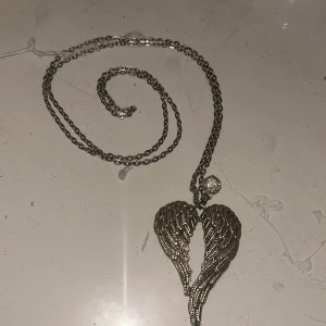 Silverfärgat halsband med änglavingar - Snyggt silverfärgat halsband med ett hängsmycke i form av detaljerade änglavingar. Väldigt fin. Lång kedja.💖
