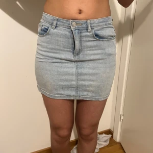 Ljusblå jeanskjol - Snygg ljusblå jeanskjol med klassisk femficksdesign och knappgylf. Perfekt för en avslappnad stil. Passar bra till en enkel t-shirt eller en somrig topp. Midjemått tvärsöver 35cm