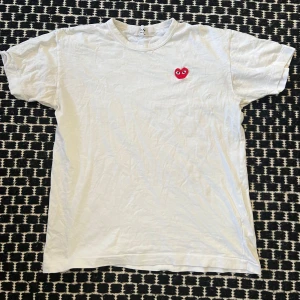 Comme des Garçons play t-shirt - Säljer en vit t-shirt från Comme des Garçons med det ikoniska röda hjärtat broderat på bröstet. T-shirten har en klassisk passform och är kortärmad. Perfekt för en stilren och enkel look. size xl men passar ~m-l