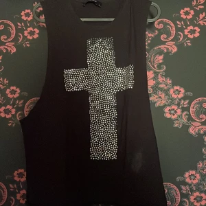 Svart ärmlös topp med strasskors  - Snygg svart ärmlös topp från Sisters Point med ett stort kors av strass på framsidan. Perfekt för en cool och edgy stil. Toppen är i en bekväm passform och passar bra till både jeans och kjol.