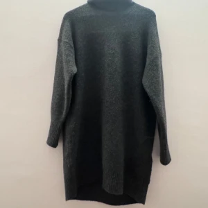 Grå stickad Klänning  - Säljer en mysig grå stickad kläning  med långa ärmar. Perfekt för kyliga dagar med sin höga krage och mjuka material. klänningen har en avslappnad passform och ribbade detaljer vid ärmslut och nederkant.