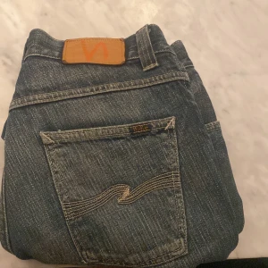 Blå jeans från Nudie - Snygga blå jeans från Nudie med klassisk femficksdesign och broderad bakficka. Jeansen har en normal passform och är tillverkade i slitstarkt denim. Perfekta för en avslappnad stil.