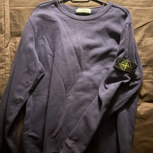 Mörkblå tröja från Stone Island - Säljer en snygg mörkblå tröja från Stone Island med deras ikoniska märke på ärmen. Tröjan har en klassisk rund hals och långa ärmar. Perfekt för en stilren look.