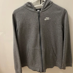 Grå hoodie från Nike - Säljer en klassisk grå hoodie från Nike med dragkedja och huva. Tröjan har långa ärmar. Jätte bra skick som ny. Nypris 850kr