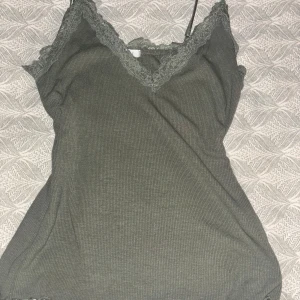Grön ribbad linnetopp med spetsdetaljer - Snygg grön ribbad linnetopp med spetsdetaljer vid halsringningen. Perfekt för sommaren! Toppen har smala axelband och en v-ringning.I storlek M men passar mig som är S.