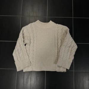 Vit stickad tröja från Gina Tricot - Säljer en mysig vit stickad tröja från Gina Tricot med flätstickat mönster. Tröjan har långa ärmar och en ribbad krage. Använd ca 2 gånger så som ny