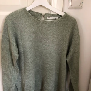 Grön stickad tröja från Sfera Basic - Säljer en stilren grön stickad tröja från Sfera Basic. Tröjan har en rund halsringning och långa ärmar. Den har en liten knappdetalj i nacken för en extra touch. Perfekt för kyligare dagar!