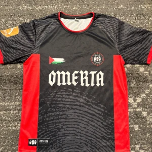 Omerta t-shirts  - Snygg fotbollströja från Omerta i svart med röda detaljer. Tröjan har korta ärmar och ett unikt mönster. Perfekt för fotbollsfans som vill sticka ut på planen.